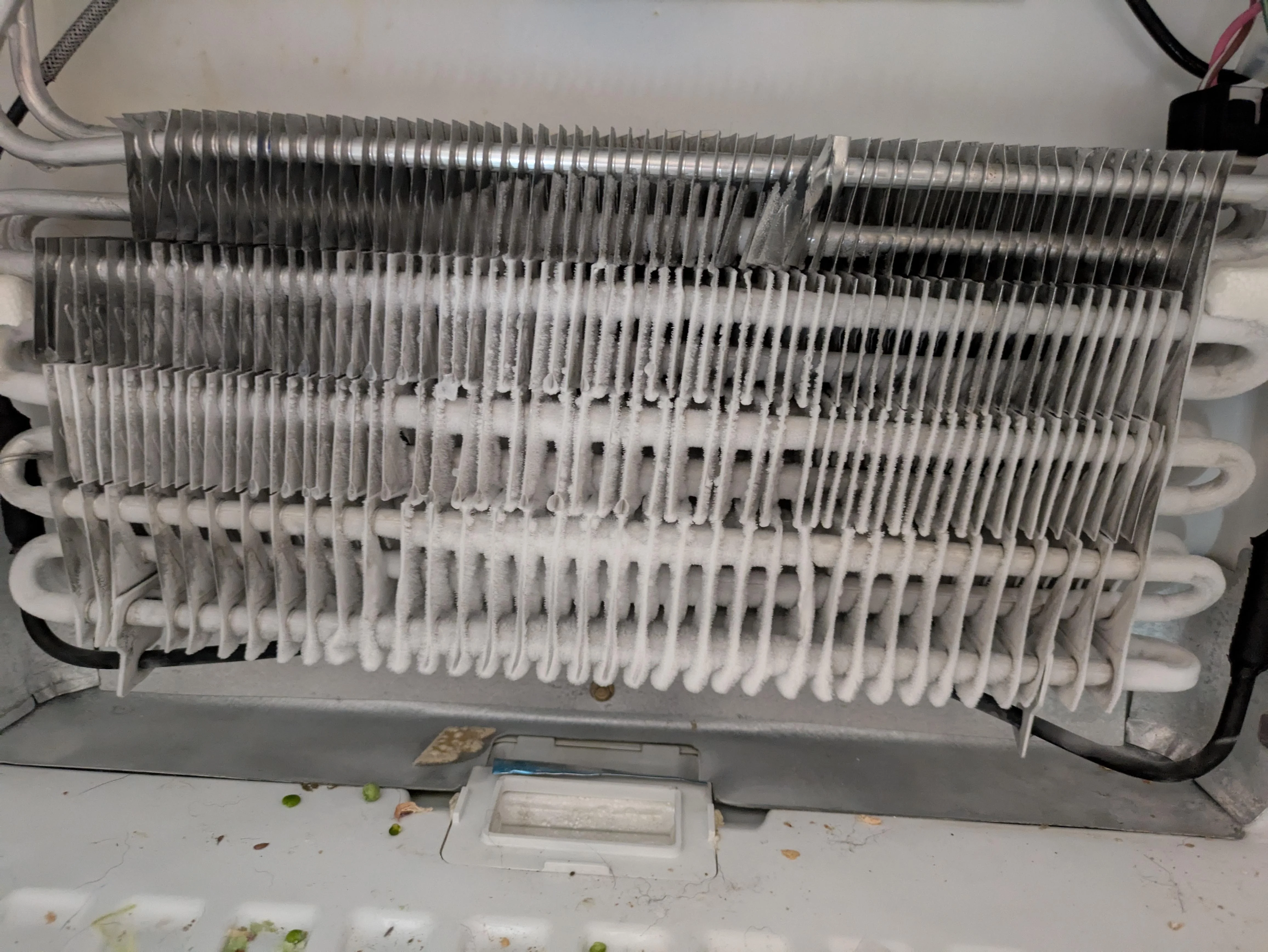 Evaporator coil behind a freezer panel showing heavy white frost buildup across the coil fins
