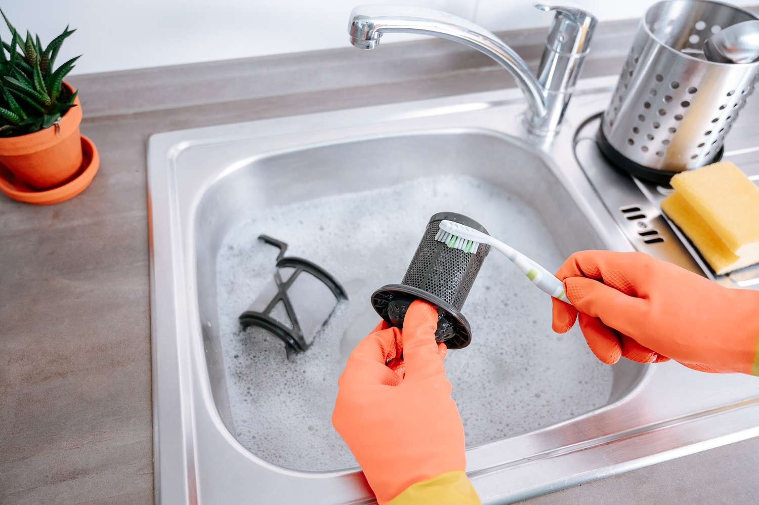 Hands lifting a cylindrical dishwasher filter out of the bottom of a dishwasher tub with water droplets, realistic photo