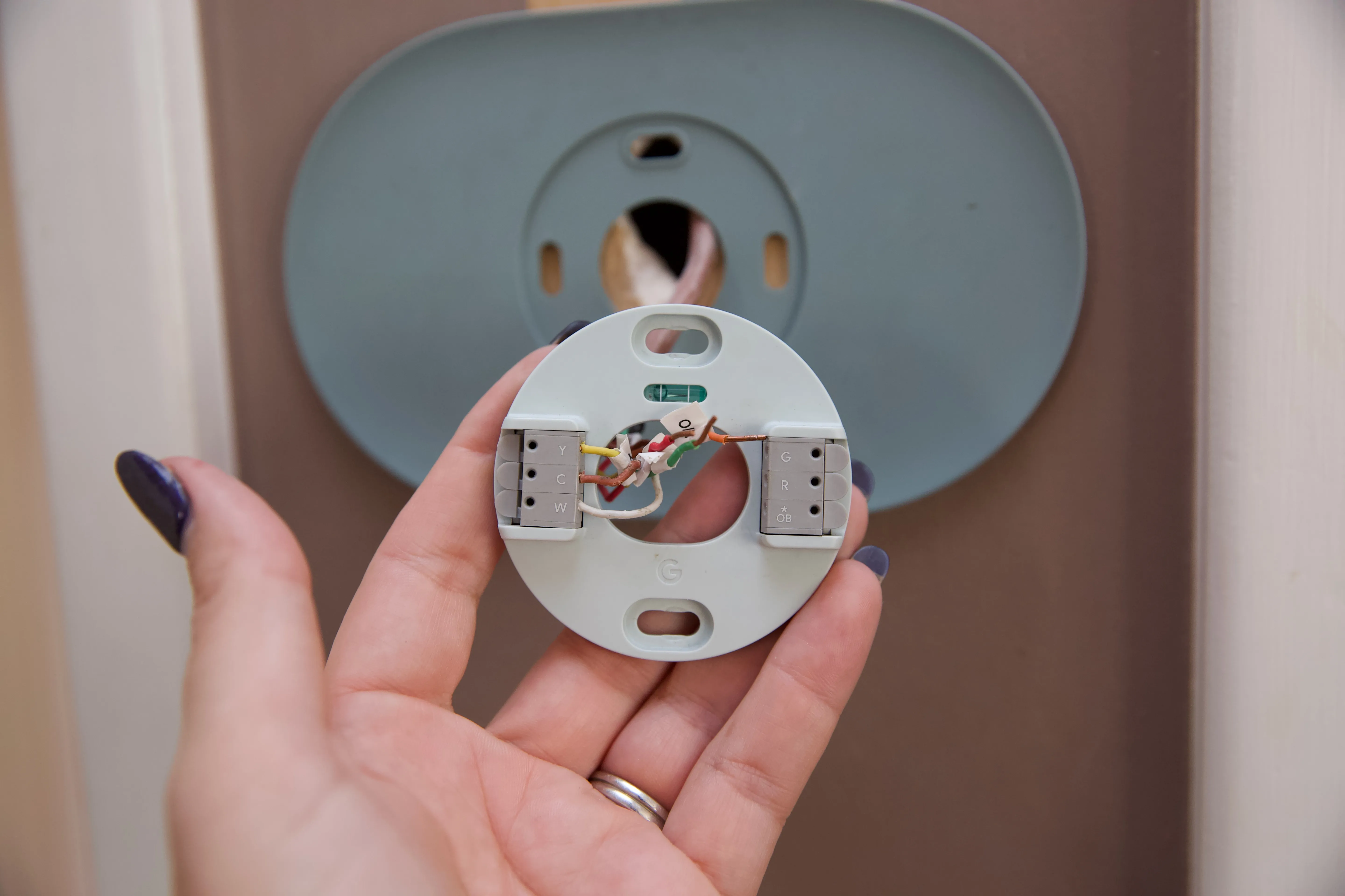 Homeowner installing a smart thermostat base with colored wires visible