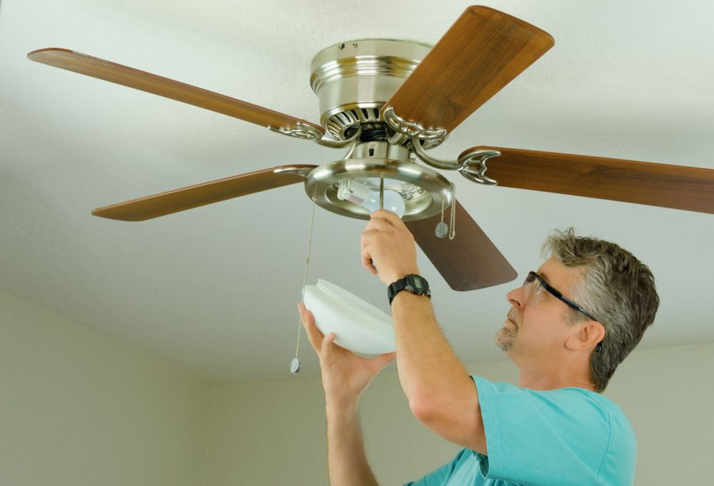 Homeowner on a step ladder inspecting a ceiling fan with the light off