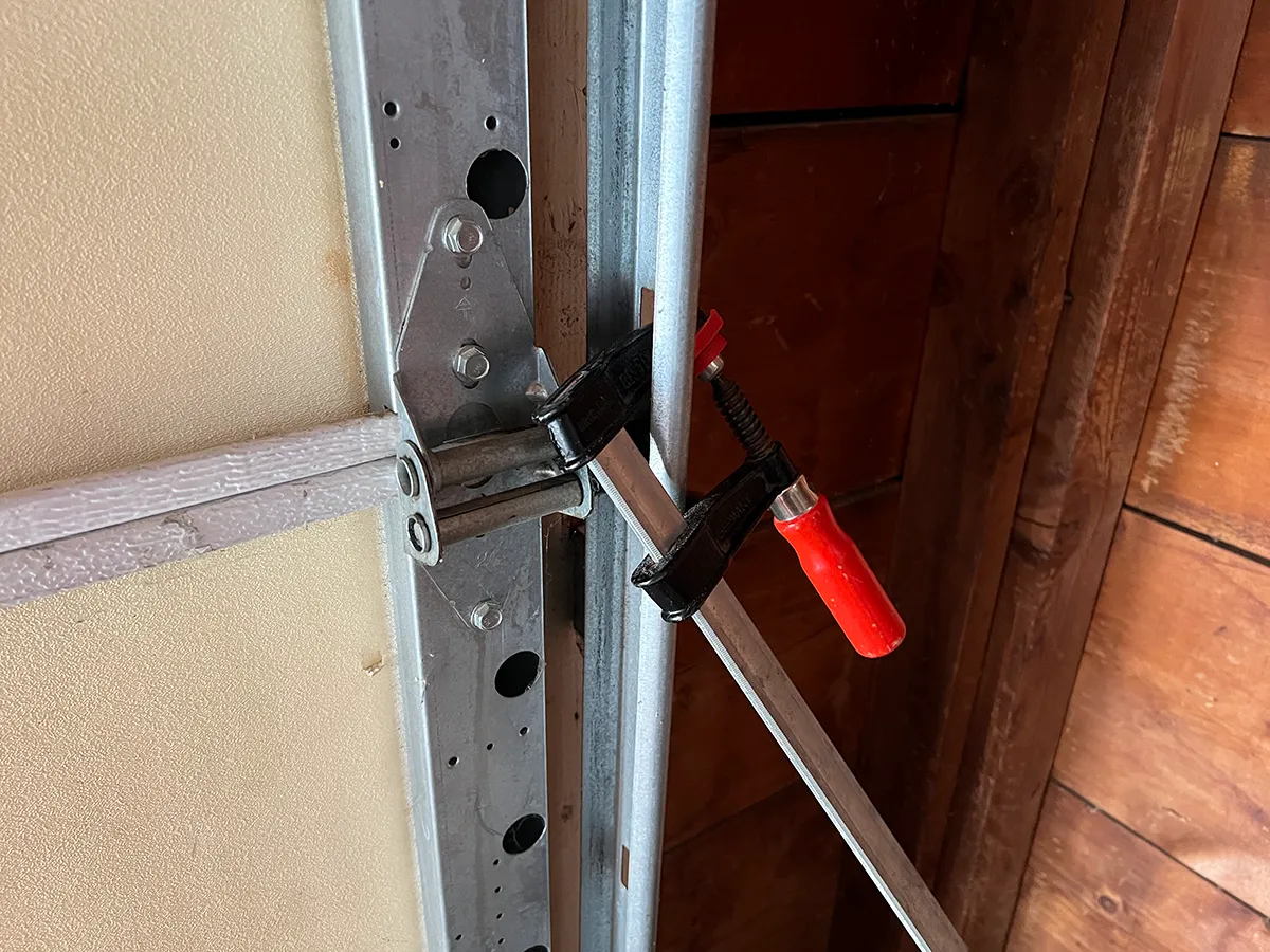Locking pliers clamped onto a garage door track just above the bottom roller to prevent the door from moving