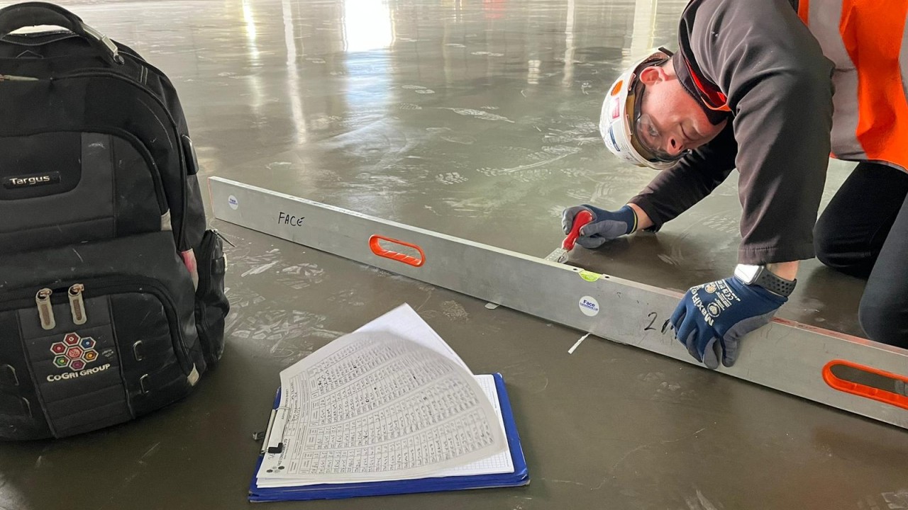 Photo of a long level laid on a vinyl plank floor with a visible gap under the center, showing a low spot being checked