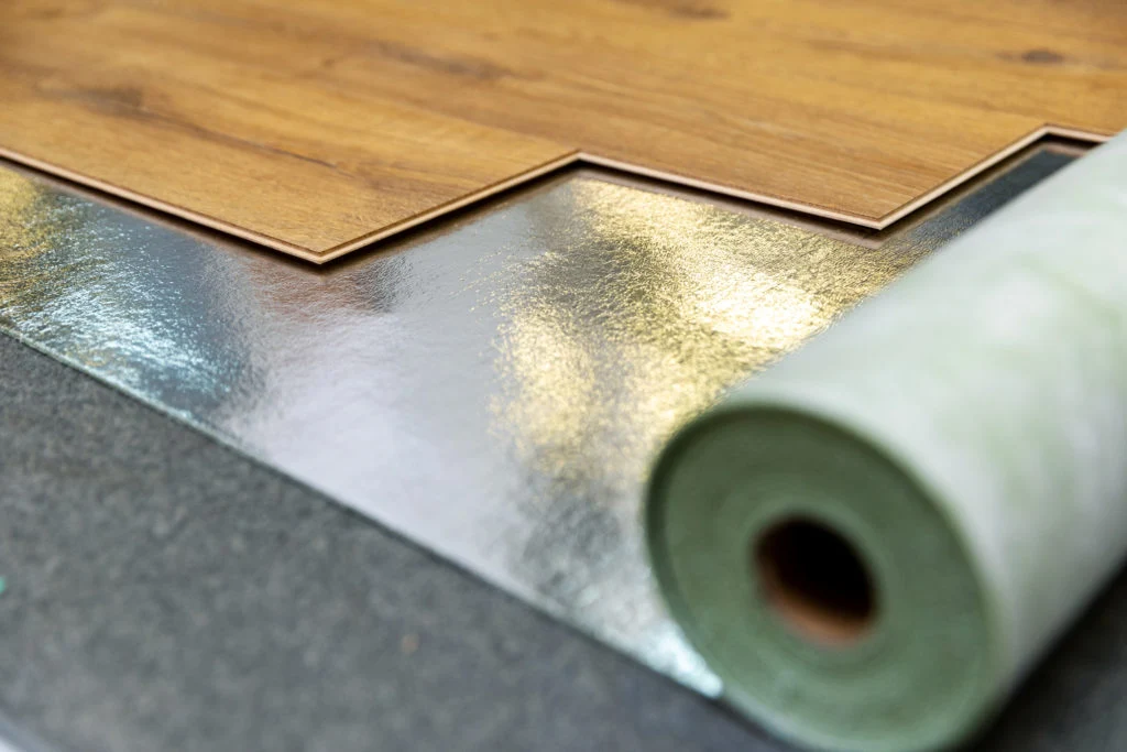 Photo of foam underlayment being rolled out on a subfloor next to boxes of click-lock vinyl plank