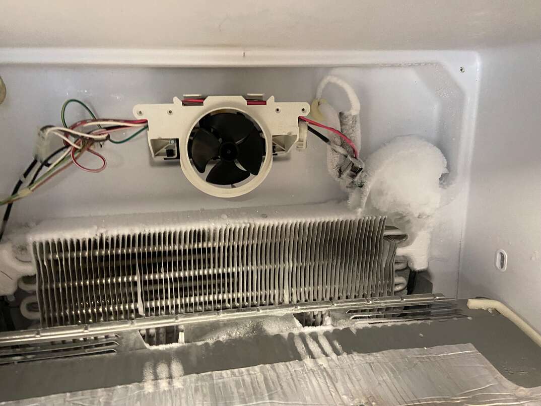 The inside of a freezer with the rear interior panel removed, showing the evaporator fan assembly and wiring harness, photographed with a handheld flashlight