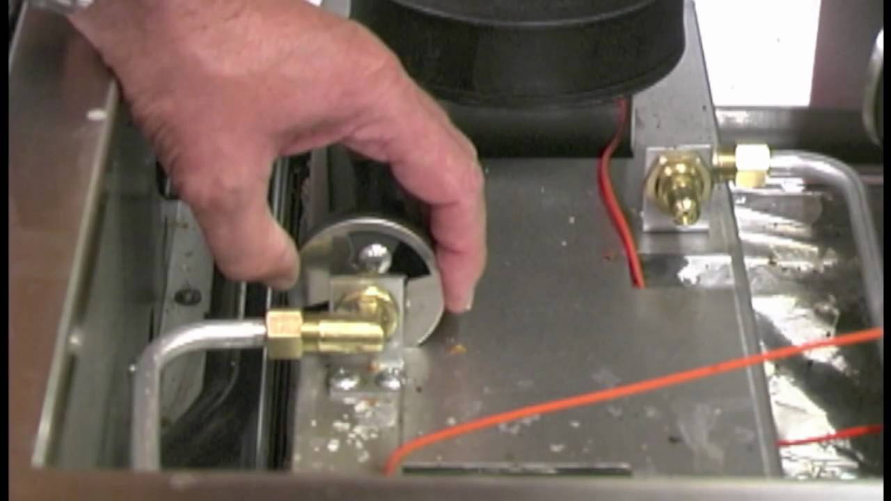 The underside of a gas range cooktop showing an adjustable air shutter collar on a burner tube with a small screw